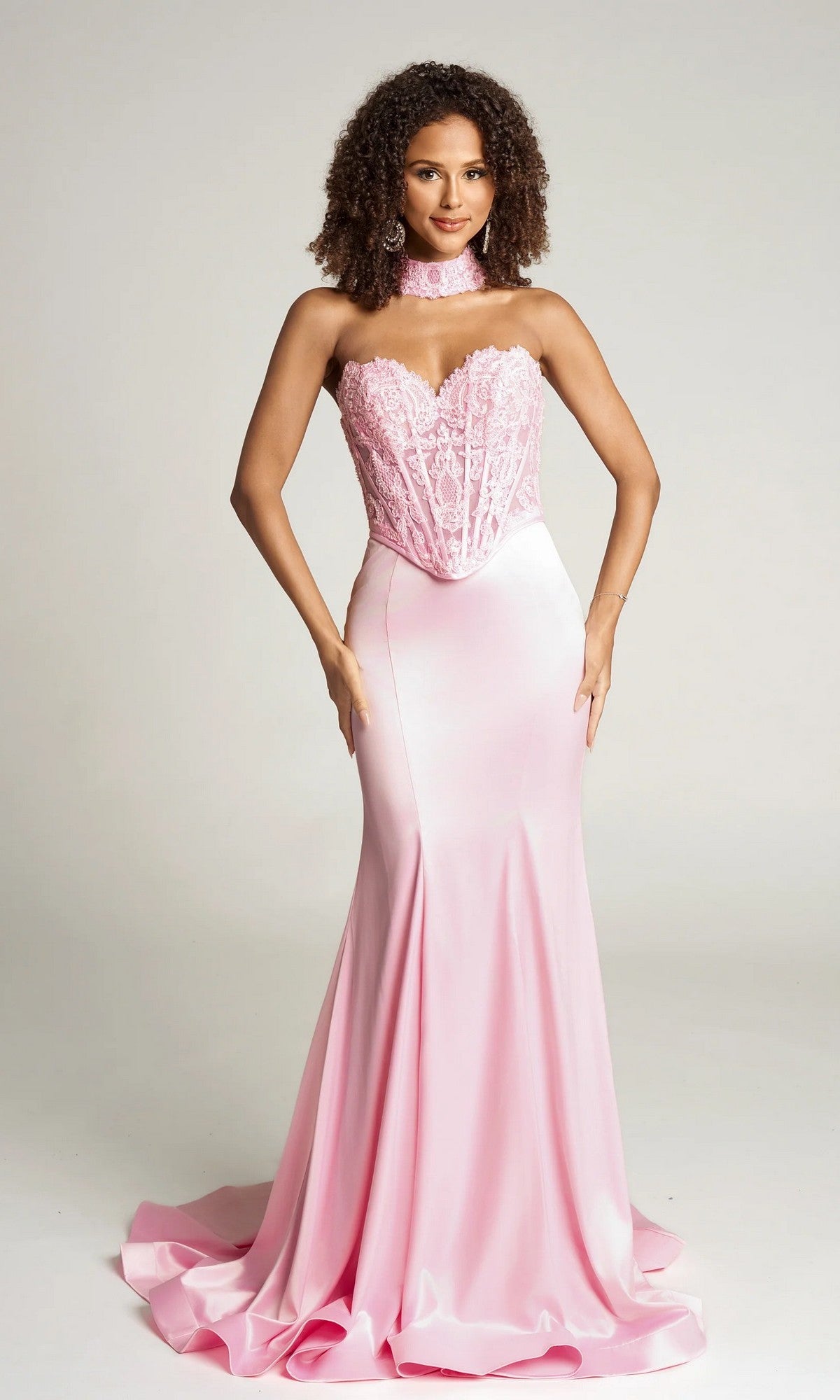A woman wears the Portia and Scarlett PS26086 long formal dress in baby pink, featuring a strapless satin design with a lace corset bodice and matching lace choker, set against a plain background.